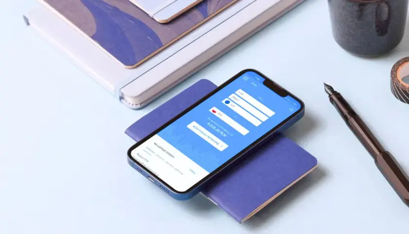 Smartfon z aplikacją do wymiany walut HKD na PLN, obok pióro i notatniki.